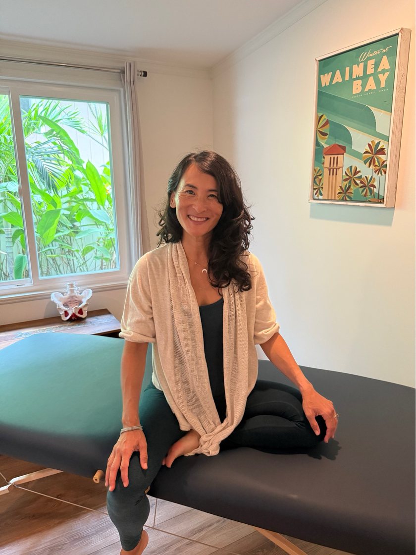 Dr. Moon, DPT, sitting on the treatment table in her private studio, with a pelvic model on the windowsill behind her.